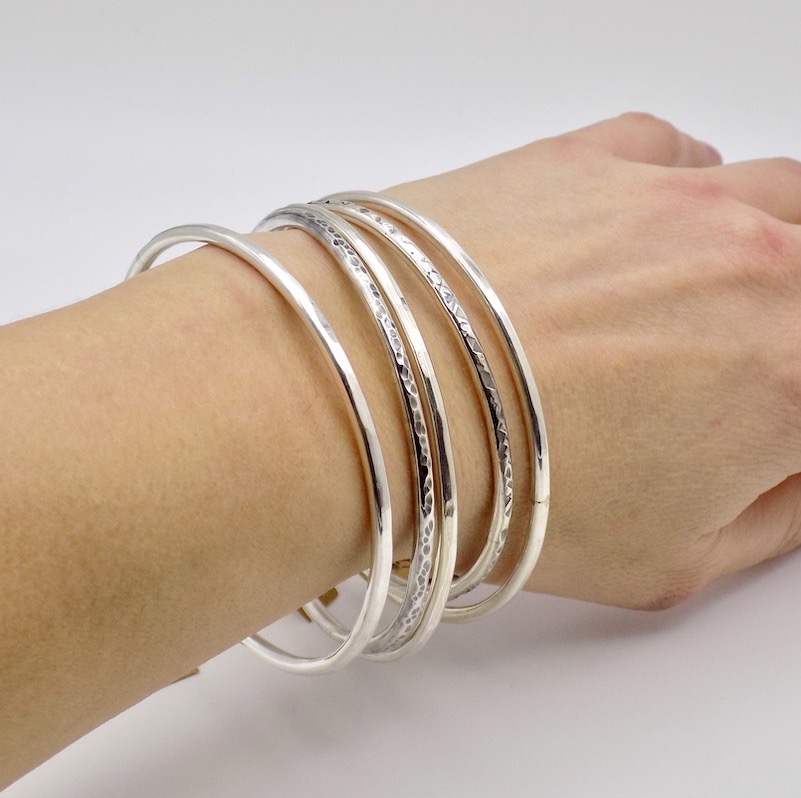 Photo d'un avant bras sur fond bland portant différents bracelets fermés en argent massif.