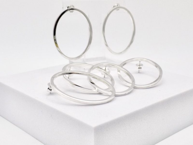 Photo de trois paires de boucles d'oreilles de forme ovale. Les boucles sont en argent massif posées sur un support blanc carré.