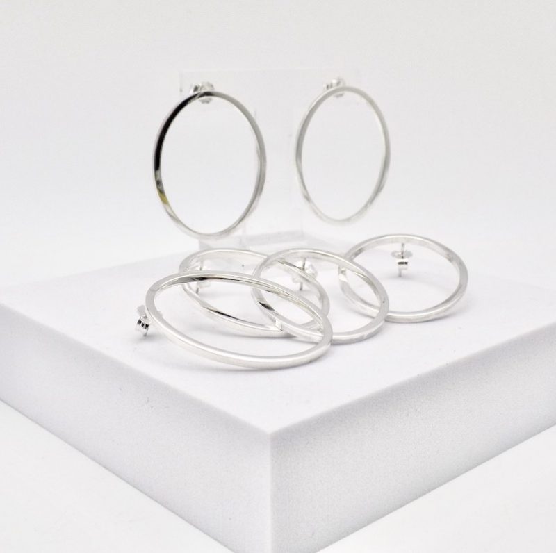 Photo de trois paires de boucles d'oreilles de forme ovale. Les boucles sont en argent massif posées sur un support blanc carré.