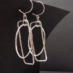 photo d'une paire de boucles d'oreilles martelée faite à partir de fil d'argent. Elles sont posées sur un fond noir.