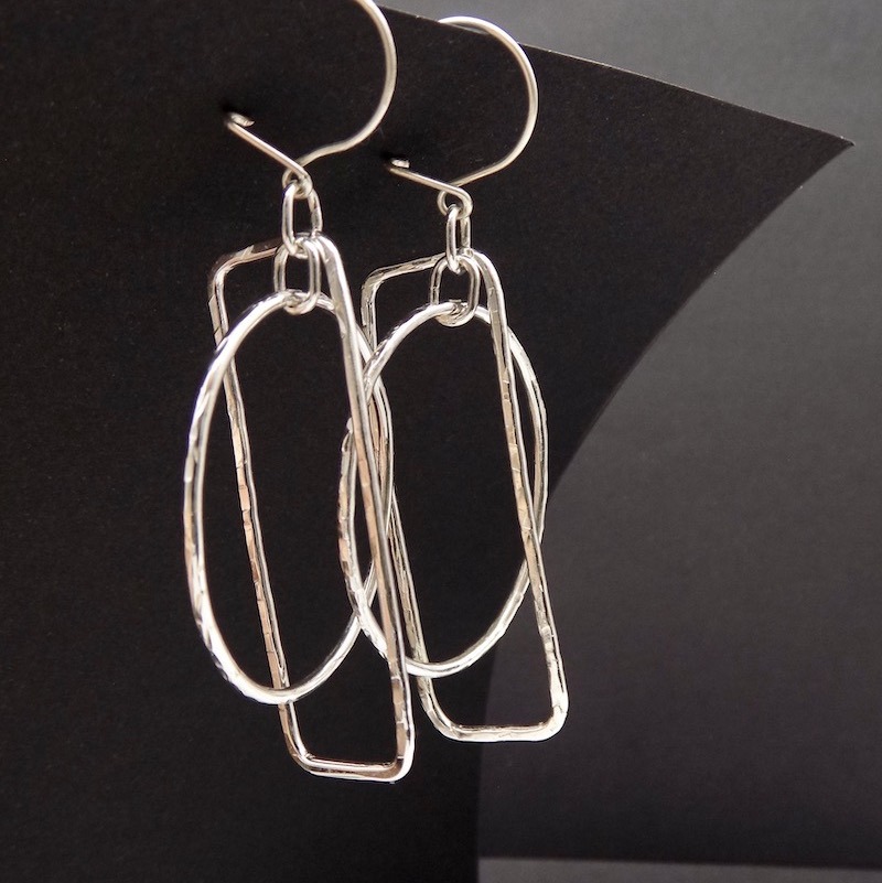photo d'une paire de boucles d'oreilles martelée faite à partir de fil d'argent. Elles sont posées sur un fond noir.
