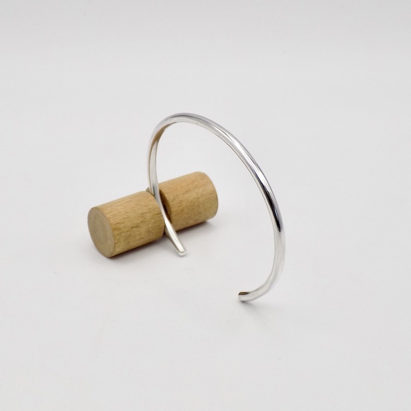 Photo d'un bracelet jonc en argent. Le bracelet est posé sur un support en bois clair.