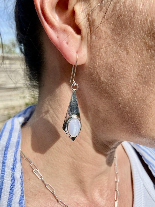 photo d'une oreille de femme portant une boucles d'oreilles longue. la boucle est de forme losange et sertie d'une pierre bleue clair , une calcedoine.