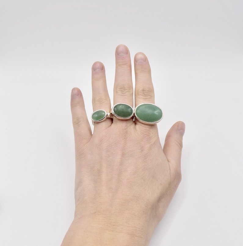 Photo d'une main qui porte trois bagues de tailles différentes. Grand, moyen, petite. Elles sont serties d'une pierre verte d'Aventurine.