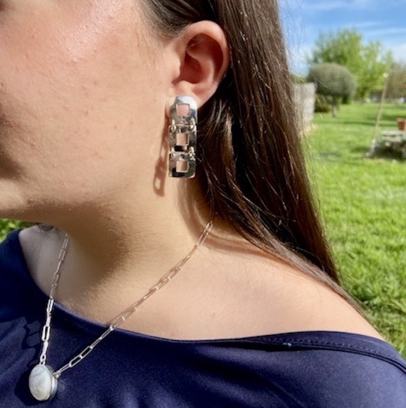 Photo de profil d'une femme portant une paire de boucles d'oreilles en argent 925. Cette paire est imposante. Elle est formée de 3 carrés évidés alignés à la vertical.