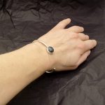 Photo d'un avant bras portant un bracelet en argent ouvert serti d'un cabochon bleu et marron de Chrysocolle de forme ronde