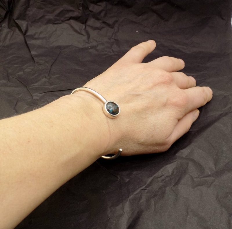 Photo d'un avant bras portant un bracelet en argent ouvert serti d'un cabochon bleu et marron de Chrysocolle de forme ronde