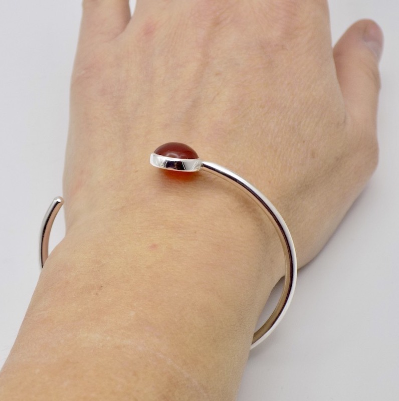 Photo d'un poignet portant un bracelet jonc ouvert. Le bracelet est serti d'une pierre orange , de la Cornaline