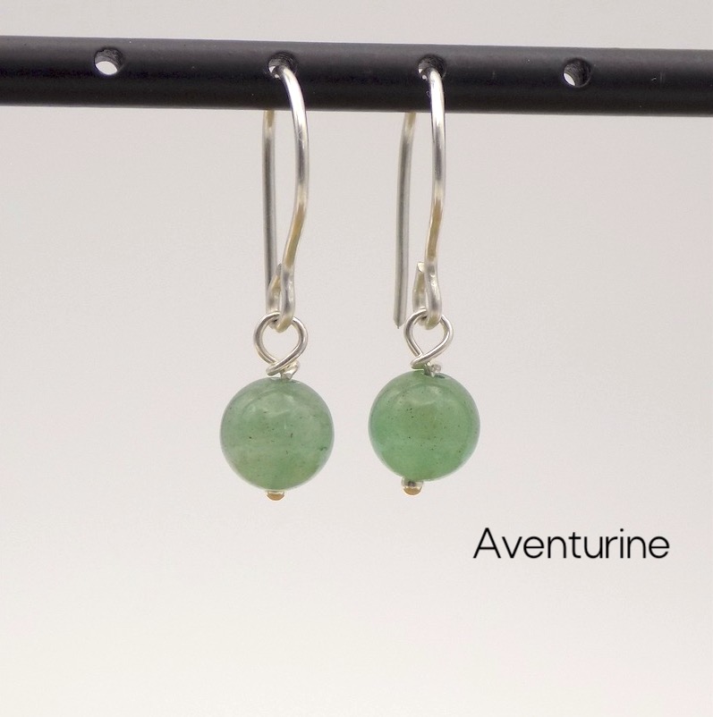 Photo d'une paire de boucles d'oreilles. Elles sont composées de petites perles rondes de pierres vertes: des Aventurine.