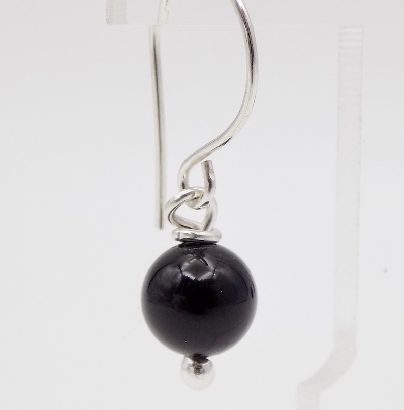 Photo d'un gros plan d'une boucle d'oreille formée d'une perle de pierre naturelle noire d'Onyx. Cette boucle se porte par une attache en argent 925 en forme de crochet