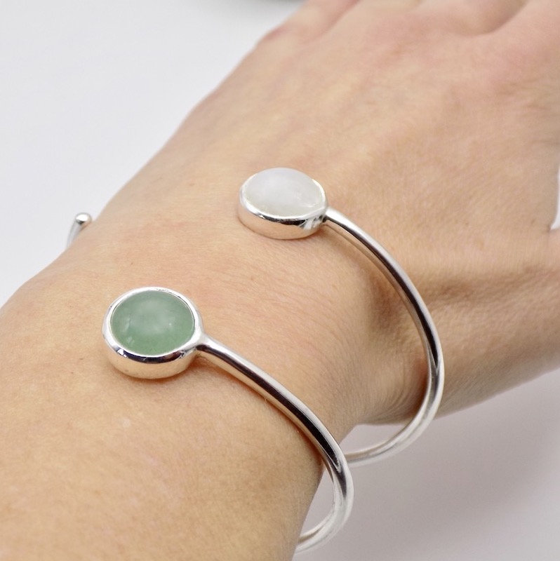 Photo d'une partie d'un poignet portant deux bracelets. Les barcelets sont chacun serti d'une pierre ronde. l'une verte, une Aventurine et l'autre blanche, une Pierre de Lune. Le bracelet est formé à partir d'un jonc en argent 925