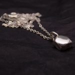 Photo d'un pendnetif en forme de pavé. il est fait tout en argent. Sur la photo il est posé sur un fond noir avec sa chaine en argent aussi.