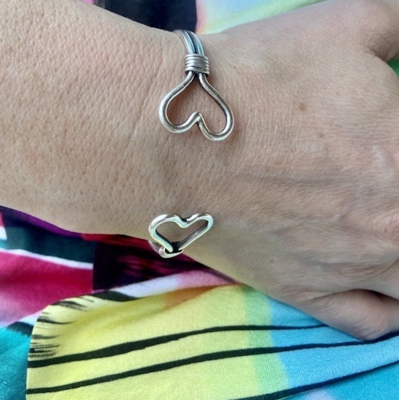 Photo en couleur d'un poignet portant un bracelet formé de deux joncs en argent. Ces joncs se finissent par un coeurs.