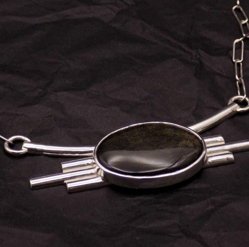 Photo de dessus d'un collier imposant en argent masif serti d'une magnifique pierre noir-dorée: une obsidienne dorée.