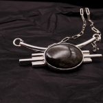 Photo d'un collier assez gros serti d'un magnifique cabochon noir doré: une obsidienne dorée. Ce collier est comme un plastron tout en argent massif.