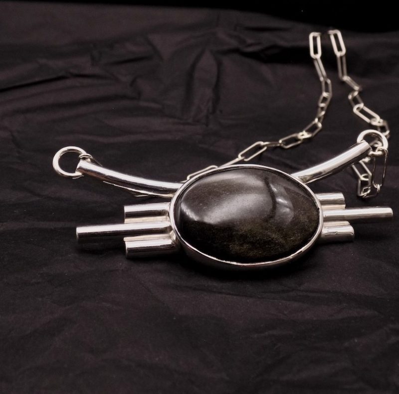 Photo d'un collier assez gros serti d'un magnifique cabochon noir doré: une obsidienne dorée. Ce collier est comme un plastron tout en argent massif.