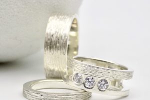 Photo de trois bagues en argent. Deux alliances et une bague de fiançailles serties e trois brillants.