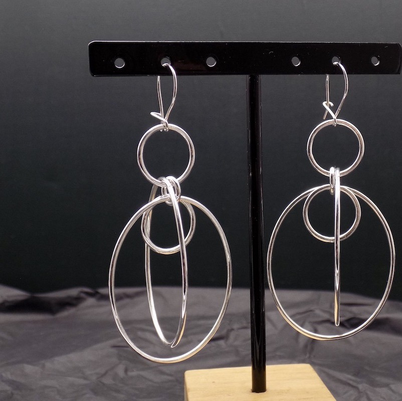 Photos de boucles d'oreilles longues en argent. Elles sont mises sur un présentoir. On peut y voir la paire.