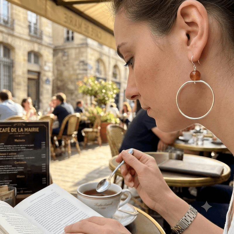 Photo d'une femme assise à un café portant une boucles longue en argent avec une pierre orange de Cornaline.