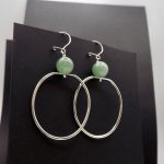 Photo d'une paire de boucles d'oreilles. Cette paire est formée de grands anneaux ovales en argent avec une perle de couleur verte claire , une pierre d'aventurine.