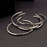 Photo prise du dessus où l'on voit plusieurs bracelets joncs ouverts en argent925 posés sur un fond noir