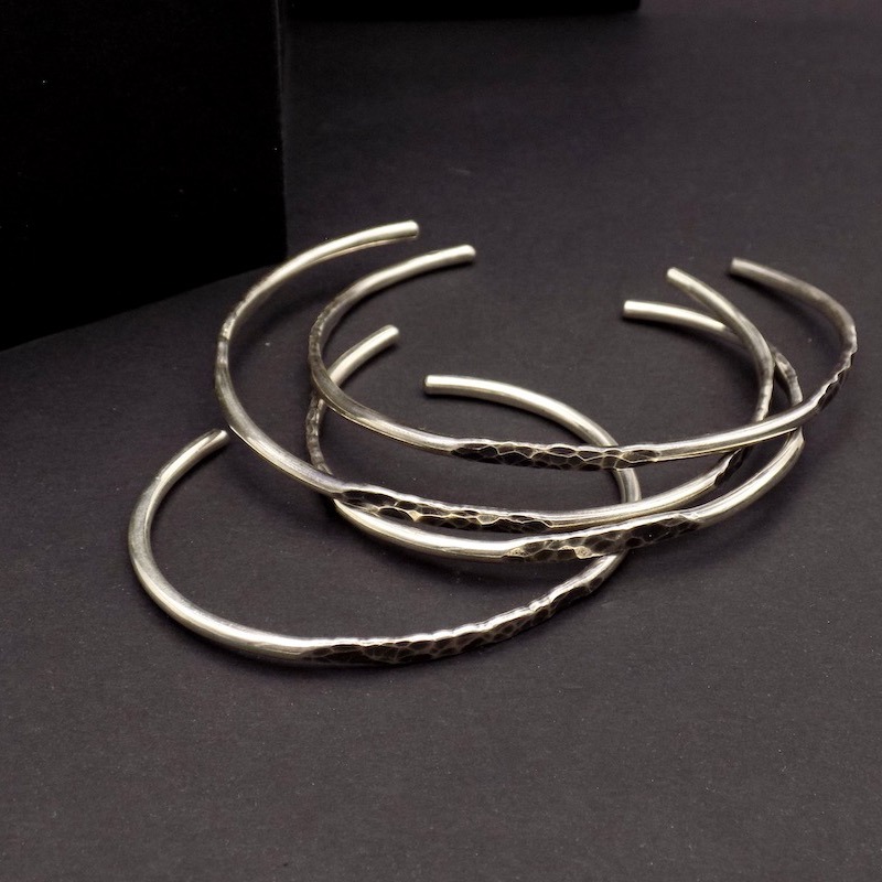 Photo prise du dessus où l'on voit plusieurs bracelets joncs ouverts en argent925 posés sur un fond noir