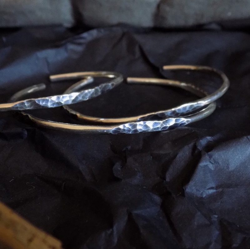 Photo assez sombre de trois bracelets en argent massif posés sur un fond noir.