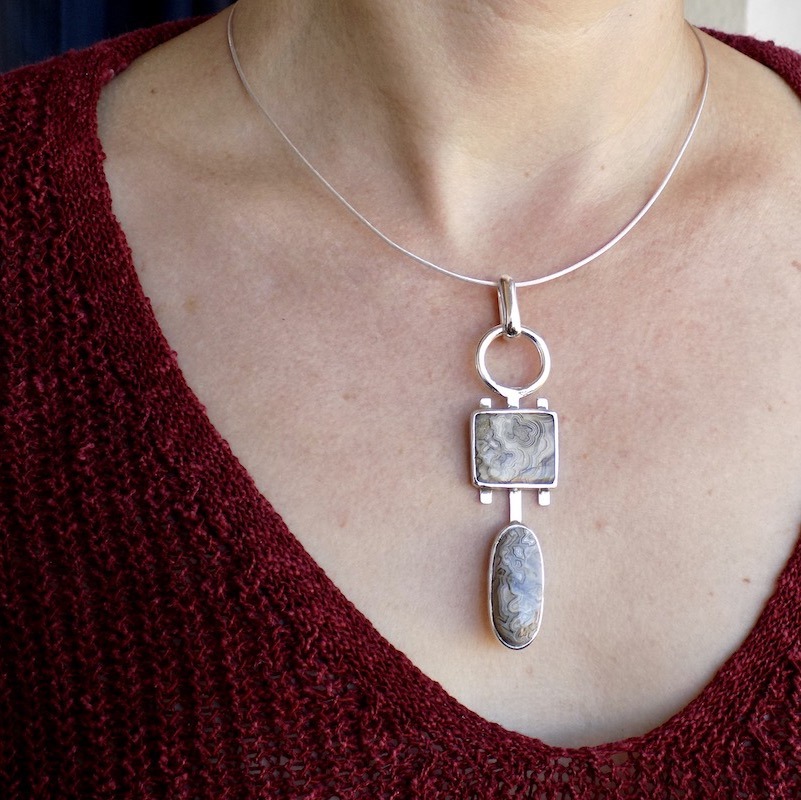 Photo d'un buste de femme portant un pendentif. Ce pendentif est longiligne fait de deux pierres d'agate crazy lace . L'une ovale et l'autre carrée.