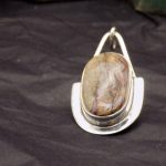 Photo d'un pendentif avec pierre posé sur un fond noir. Le pendentif est de forme ovale ainsi que la pierre sertie.