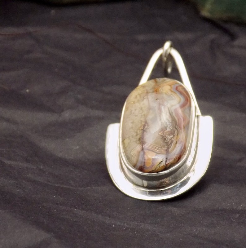 Photo d'un pendentif avec pierre posé sur un fond noir. Le pendentif est de forme ovale ainsi que la pierre sertie.