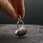 Photo d'un pendentif tenu par une main. Ce pendentif est une pierre de couleur bleue et marron .