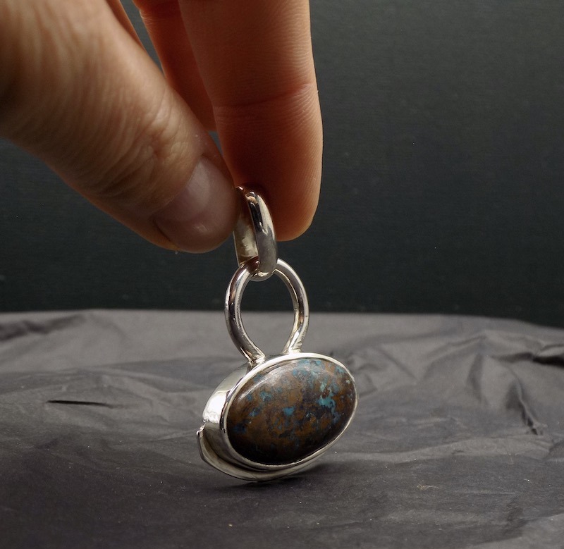 Photo d'un pendentif tenu par une main. Ce pendentif est une pierre de couleur bleue et marron .