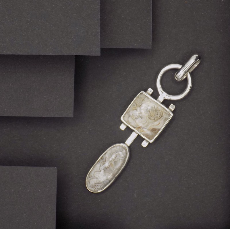 Photo prise d'un point de vue haut sur un pendentif fait en argent 925 et de deux cabochons de pierres d'agate crazy lace. Cette pierre sont de couleurs marron-beige-crème.