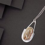 Photo couleur d'un pendentif au design moderne. Ce bijou est fabriqué en argent 925 et serti d'une pierre ovale d'agate bubble. La couleur est de crème-marron-brun.