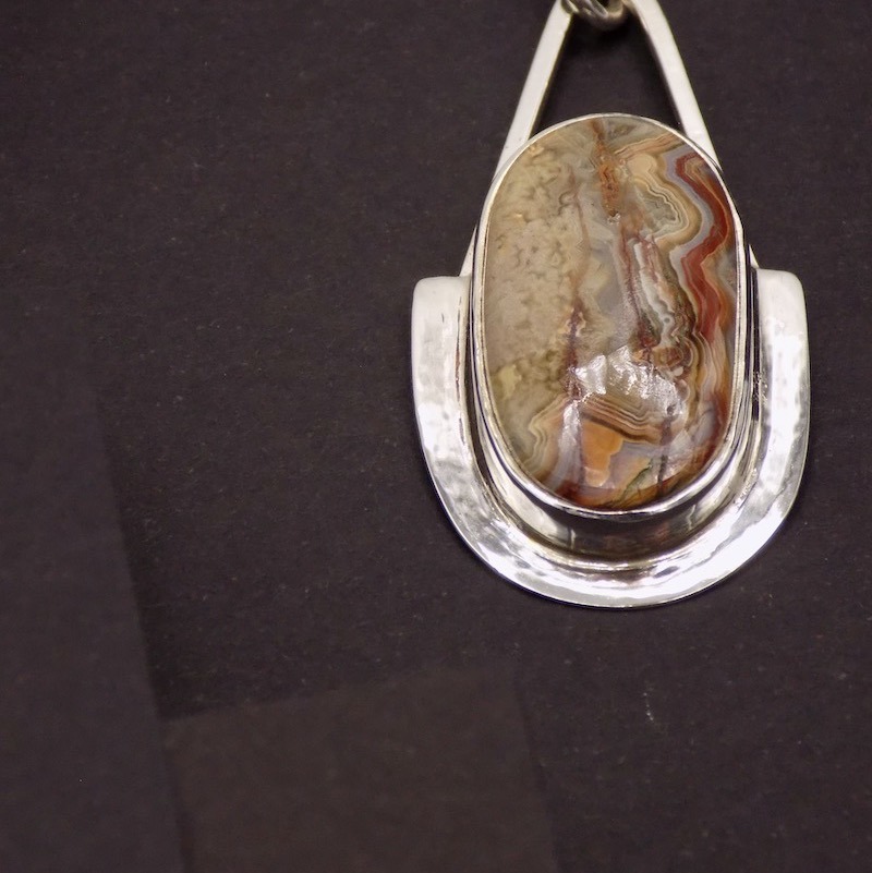 Photo couleur en gros plan de la pierre qui est sertie sur un pendentif en argent. La pierre est une agate bubble et ses couleurs sont du marron-brun-rouge
