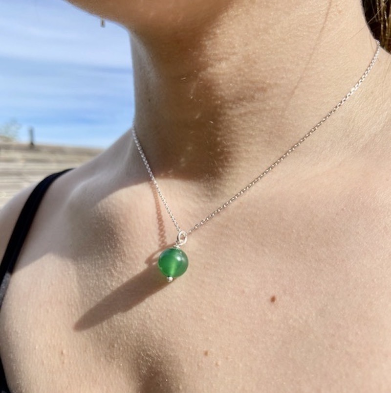 Photo gros plan en couleur d'un décolleté féminin portant une perle d'agate verte en pendentif.