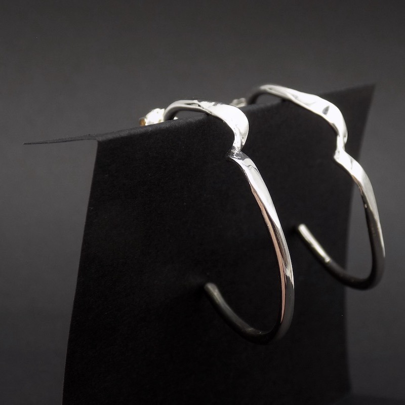 Photo montrant le profil d'une paire de boucles d'oreilles posées sur un carton noir. Paire de créole.