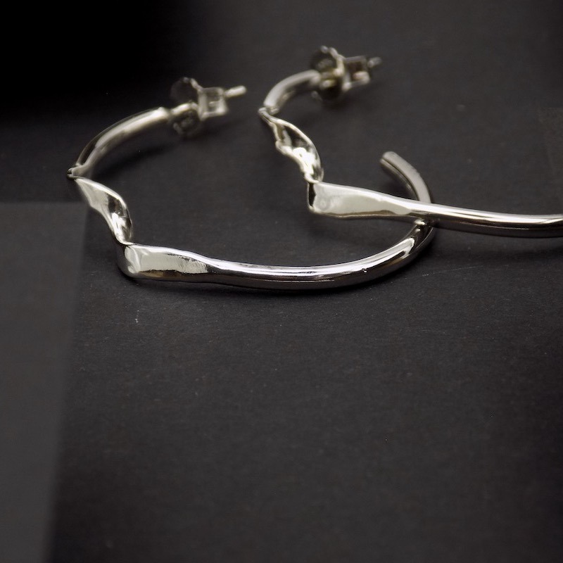 Photo d'une paire de créole en argent posée sur fond noir.