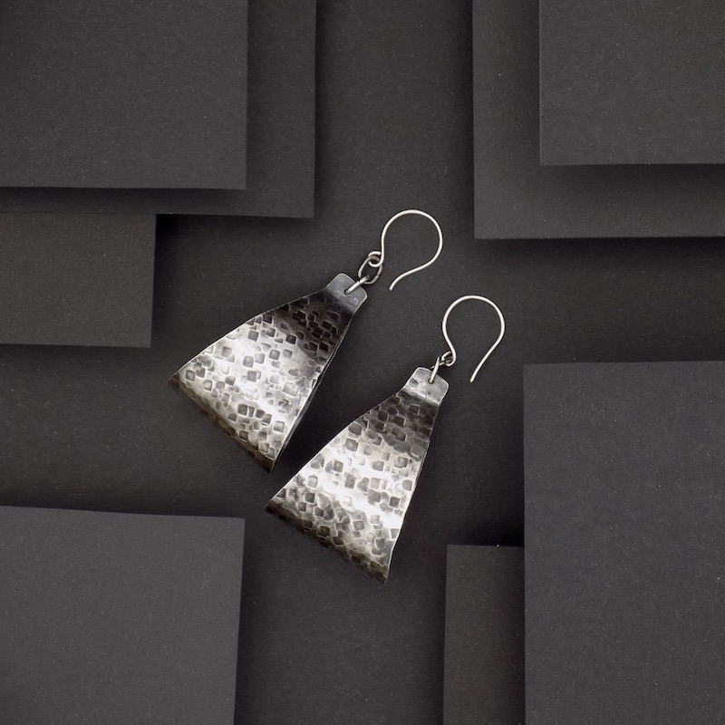 Photo vue de dessus d'une paire de de grandes et grosse paire de boucles d'oreilles. ces boucles sont en argent martelé puis oxydé ce qui leur donne un air vieilli.