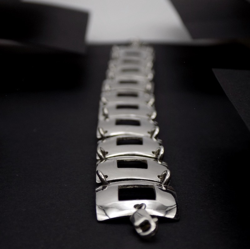 Photo foncée d'un bracelet en argent. La photo est une vue plongeante sur la longueur du bracelet. On voit bien le premier plan tandis que le second plan est flou.