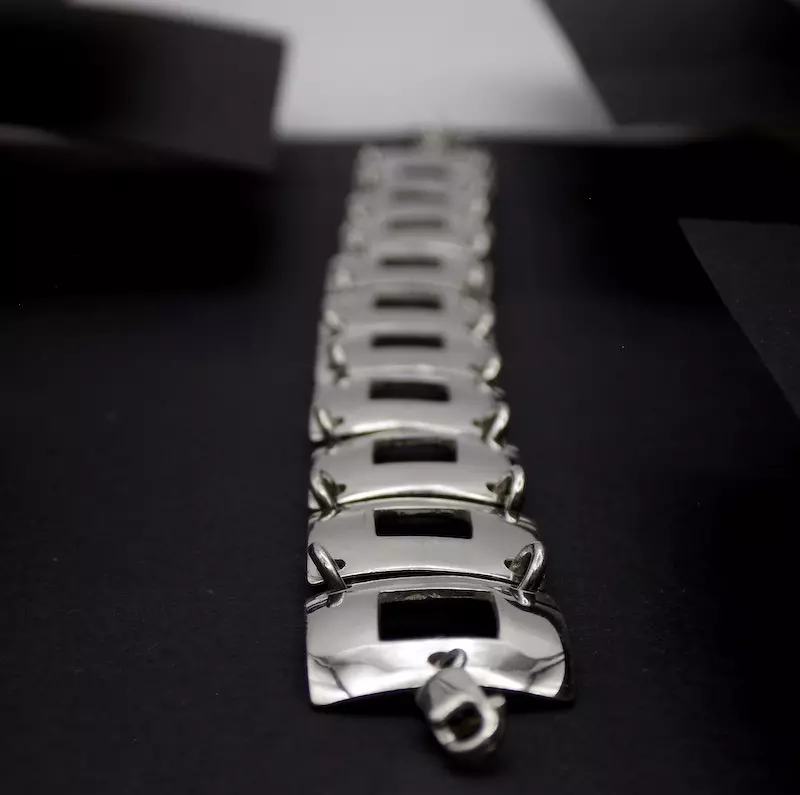 Photo foncée d'un bracelet en argent. La photo est une vue plongeante sur la longueur du bracelet. On voit bien le premier plan tandis que le second plan est flou.