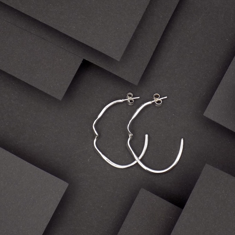 Photo d'une paire de boucles posées sur un fond noir. Paire de créole en argent.