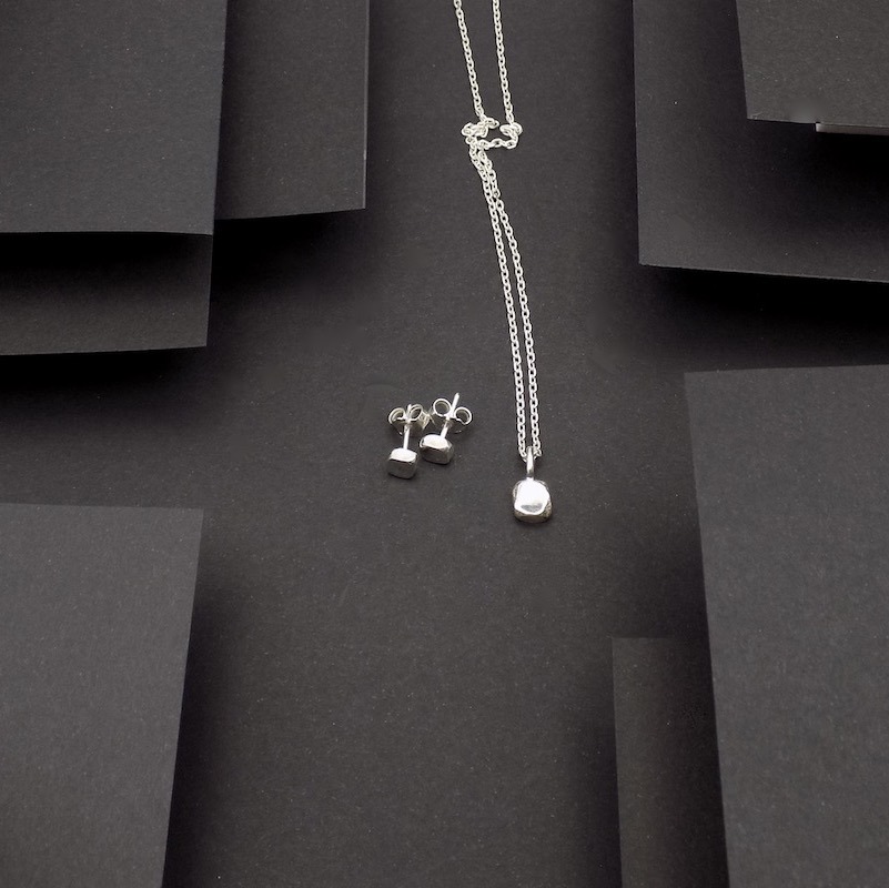 Photo prise de haut afin de voir un duo boucles -pendentif. Ces bijoux sont de petits pavés fait en argent massif.