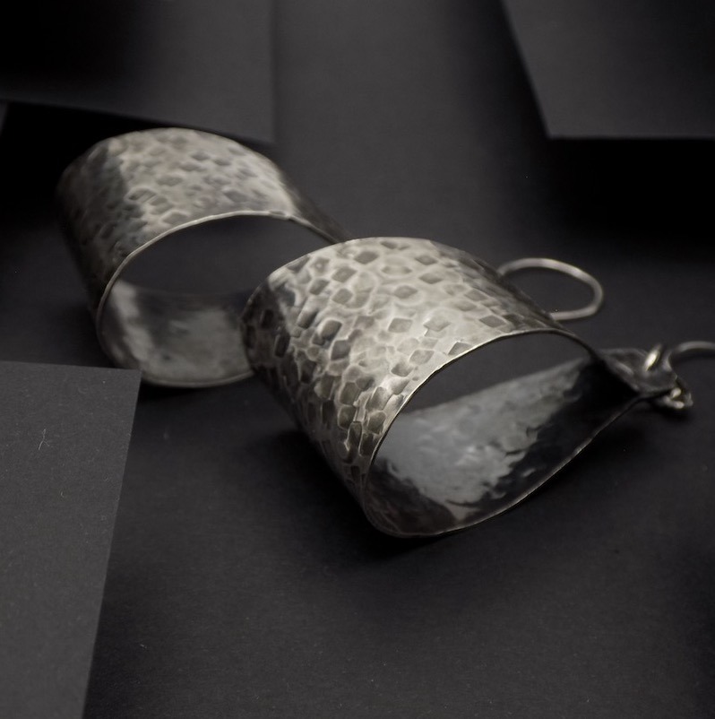 Photo vue de profil du paire de boucles d'oreilles. La photo est sur sur fond noir pour faire ressortir l'argent martelé.