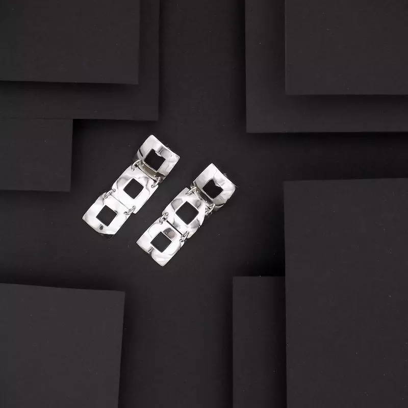 Photo vue de dessus d'une paire de boucles d'oreilles très design. Formées de trois carrés ajourés ce sont des bijoux réalisés artisanalement et en argent massif.
