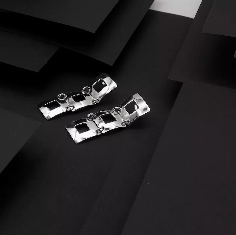 Photo faite sur fond noir pour faire ressortir une paire de boucles d'oreilles en argent. Ce sont des boucles formées de trois carrés ajourés accrochés ensemble l'un derrière l'autre