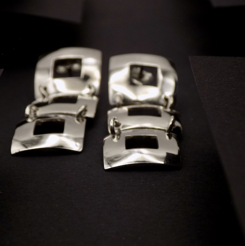 Photo prise de face d'une paire de boucles d'oreilles formée par trois carrés ajourés alignés l'un derrière l'autre. Cela leur donne un style très distingué.