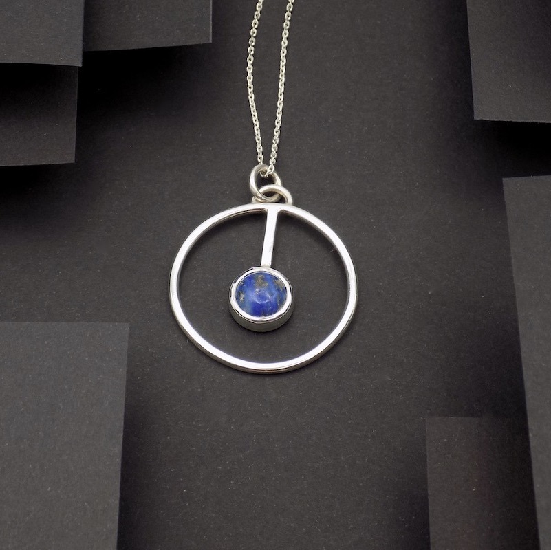 Photo sur fond noir d'un pendentif rond serti d'une pierre de lapis lazuli.