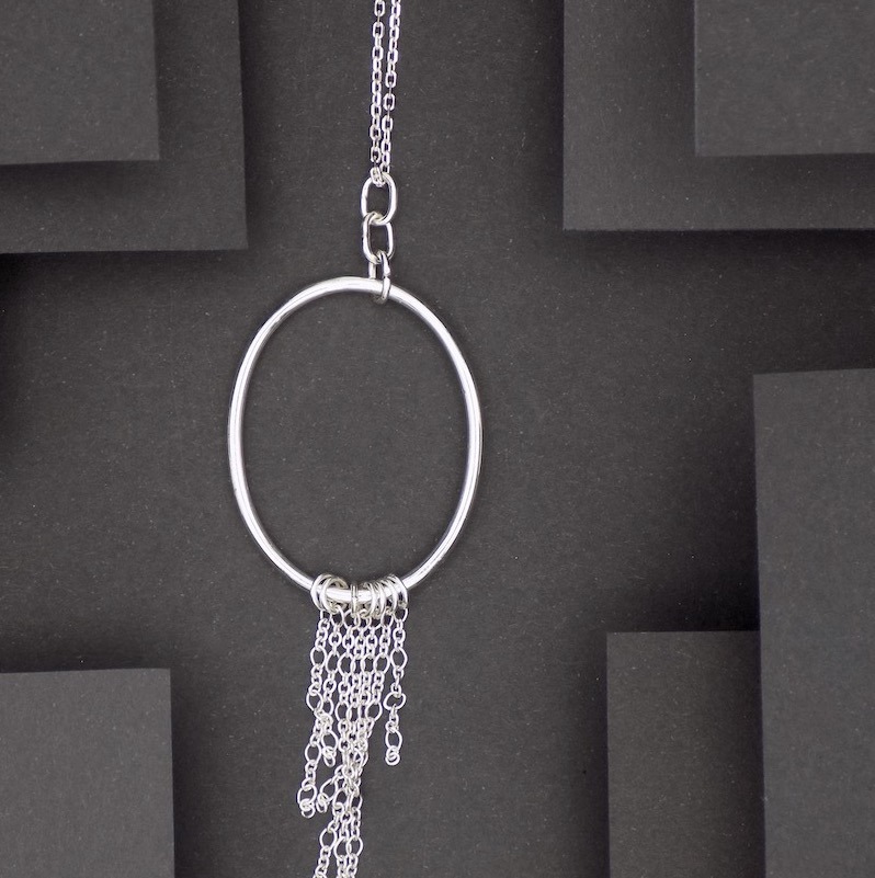Photo prise de haut montrant un pendentif formé d'un anneau auquel est suspendu plusieurs chaines de différentes longueurs. Cela ressemble comme une méduse.