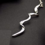 Photo d'un pendentif longiligne en argent. Le design est très contemporain. Ce pendentif est ondulé sur sa longueur comme des vagues.